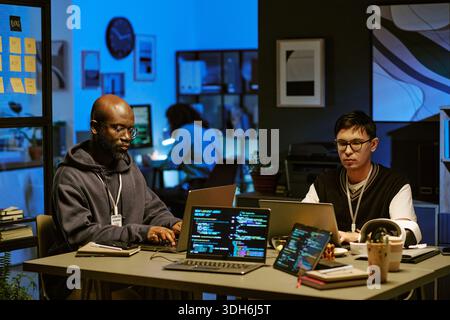 Young Adult Asian Man and Young Black Man Developing Software at Night Stock Photo