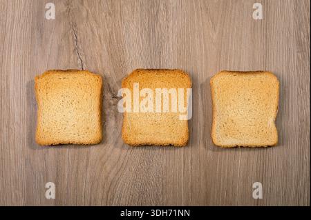 Three slices of dried bread or rusks lying flat on a light wooden background Stock Photo