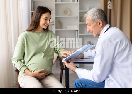 Pregnant woman reviewing medical documents with senior male doctor during prenatal consultation Stock Photo