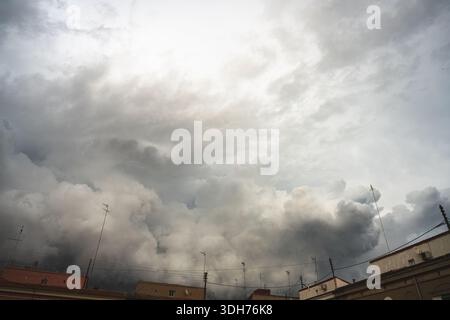 Dark storm clouds hang over the buildings. The sky is overcast, and the sun shines through the clouds. Low, dark clouds create a terrifying atmosphere Stock Photo