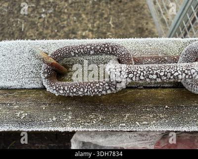 Close-up of a rusted metal chain covered in frost on a wooden fence during cold winter weather on a rural farm Stock Photo
