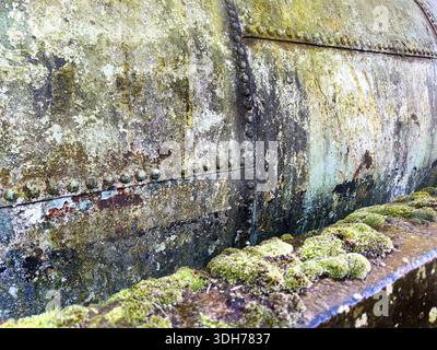 Close-up of a moss-covered rusted metal tank structure with corrosion and weathered texture suggesting long-term exposure to the elements Stock Photo