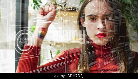 Interacting woman in red turtleneck touching transparent display at office, with digital panels Stock Photo
