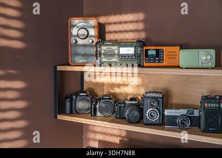 VINKOVCI, CROATIA, 10.08.2025:A warm, nostalgic display of vintage cameras and retro radios arranged on a two-tier wall shelf, creating a cozy, retro- Stock Photo