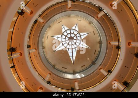 Dubai, UAE - February 1, 2023: View from below of the circular atrium ceiling at Dubai Mall, featuring a star-shaped skylight and warm lighting Stock Photo