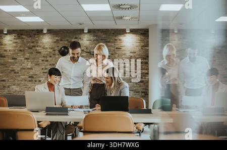 Four professionals gather around a table in a stylish office, discussing a project with documents spread out. They share ideas and collaborate effecti Stock Photo