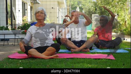 Stretching senior adults doing seated side bends on garden lawn in workoutwear, with yoga mats Stock Photo