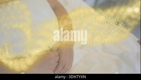 Clasping Korean couple's hands resting on white bed sheets, showing golden bokeh overlay Stock Photo