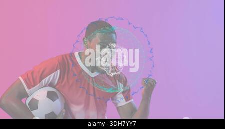 Holding soccer ball, male athlete in red soccer jersey pumping fist in studio with holographic mesh Stock Photo