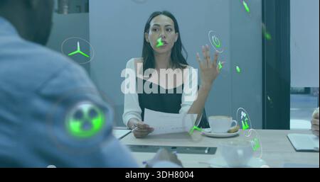 Presenting Asian woman in black blouse holding document, gesturing at meeting with green AR icons Stock Photo