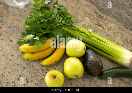 Celery, bananas, green apples, avocado and cucumber resting on granite counter, glass rim visible Stock Photo