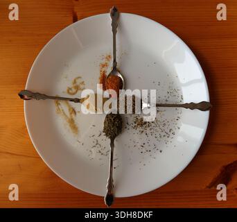Spoons with different spices. White, black and cayenne pepper, also thyme. Above angle shot on plate. Stock Photo
