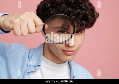 Close portrait of young man using magnifying glass for investigation verification audit research and quality control concept on pink background Stock Photo
