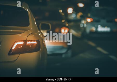 A car is parked in the middle of a busy street at night. The street is filled with other cars and the lights from the cars are reflected in the car's Stock Photo
