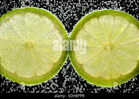Two pieces of lime with bubbles in the middle. The bubbles are floating on top of the lime slices, creating a visually appealing and refreshing scene Stock Photo