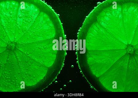 Two green lime slices with water droplets on them. The lime slices are cut in half and the water droplets are on the outside of the slices Stock Photo