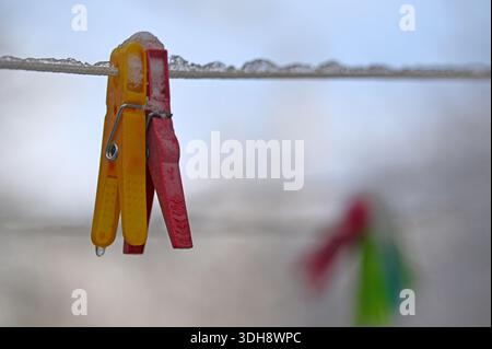 A red and yellow clothespin is hanging on a line. The clothespin is wet and has a few drops of water on it Stock Photo