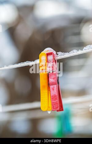 Two red and yellow clothespins are hanging on a line. The clothespins are covered in snow Stock Photo