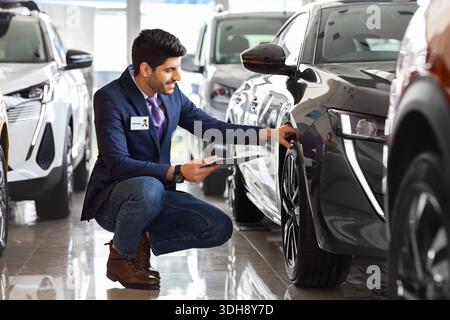 Handsome man in suit sales assistant checking car tires Stock Photo