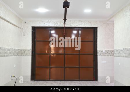 A garage with a brown door and a camera on the wall. The garage is empty and the door is open Stock Photo