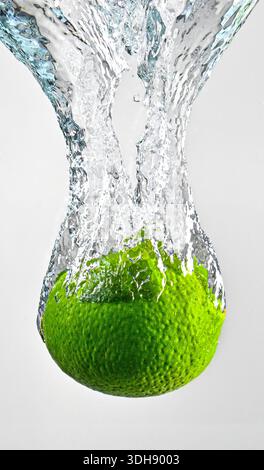 A lime is falling into a stream of water. The lime is green and the water is clear Stock Photo