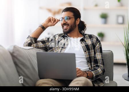 Dreamy arab guy freelancer working from home, using laptop Stock Photo
