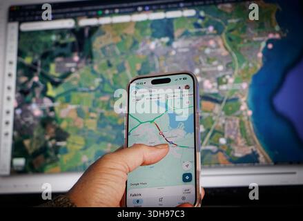 Person using navigation app on smartphone with digital map display in background showing detailed satellite imagery and road network Stock Photo