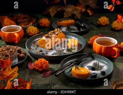 Pumpkin swiss roll and smaller rolls served with walnuts, blueberries, and tea in pumpkin shaped mugs, creating a cozy atmosphere on a fall table sett Stock Photo