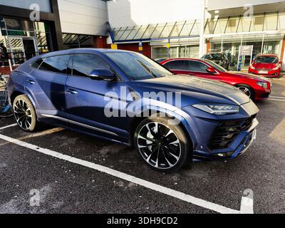 Manchester, UK - January 14, 2026: A sleek blue luxury Lamborghini Urus SUV in a parking lot near a shopping center, evoking style and power. Stock Photo