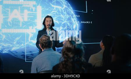 Asian public speaker makes artificial intelligence sales pitch with AI automation and big data analysis. Business forum presentation attracts investors, experts and diverse audience members. Stock Photo