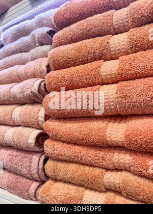 Neatly arranged towels in shades of peach and pink are stacked on a shelf, displaying soft textures and patterns in a retail setting for home textiles Stock Photo
