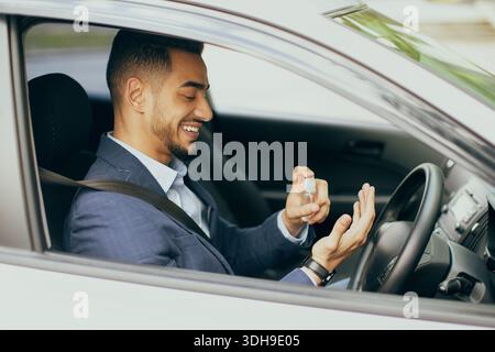 Cheerful businessman using disinfectant spray while sitting in car Stock Photo