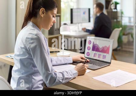 Female financial analyst working with charts on laptop in modern office interior Stock Photo