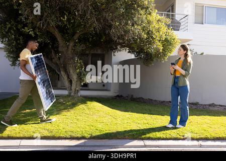 Diverse pair walking on lawn, carrying solar panel and holding tablet, copy space Stock Photo
