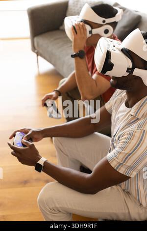 Two men are wearing white VR headsets and holding controllers in home living room Stock Photo