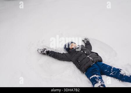 Happy child enjoying winter outdoors. Smiling boy wearing warm winter clothes and knitted hat, playing in the snow on a cold snowy day. Natural light Stock Photo