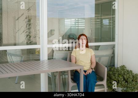 Young woman resting with eyes closed on an apartment balcony, calm outdoor home lifestyle scene. Stock Photo