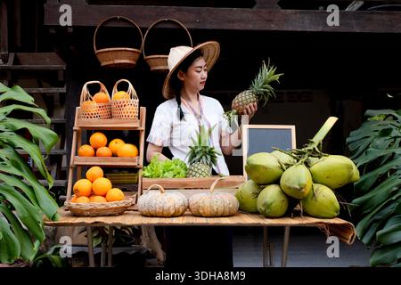 A native Asian woman holding a fresh pineapple. She sells a variety of fruits at the farm stay at Thailand Loei Stock Photo