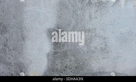 Close-up of a weathered grey concrete wall featuring a rough texture, dark damp stains, and fine surface cracks, ideal for an industrial background te Stock Photo