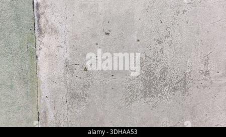 A close-up shot of a weathered, textured gray concrete wall featuring cracks, dark spots, and hints of green moss or old paint. Stock Photo