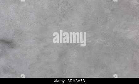 A close-up view of a grey, textured concrete wall surface, showing a fine-grained, rough plaster finish with subtle variations in color and tone. Stock Photo