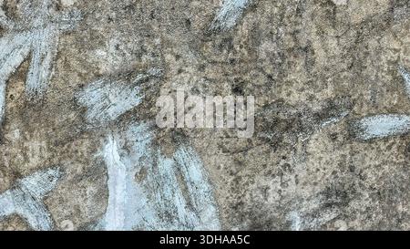 Close-up view of a rough, weathered concrete wall featuring irregular patches of faded light blue paint and dark organic staining, creating an abstrac Stock Photo