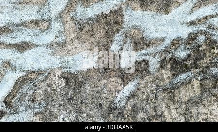 Close-up view of a rough, weathered concrete wall featuring irregular patches of faded light blue paint and dark organic staining, creating an abstrac Stock Photo