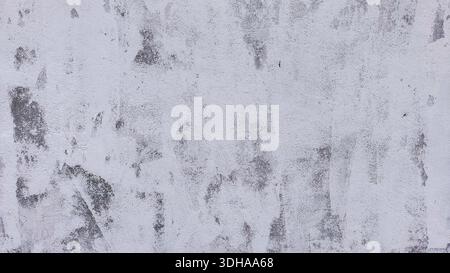 A high-resolution, close-up shot of a weathered, light-colored wall with visible gray patches, cracks, and peeling paint, creating a gritty, industria Stock Photo