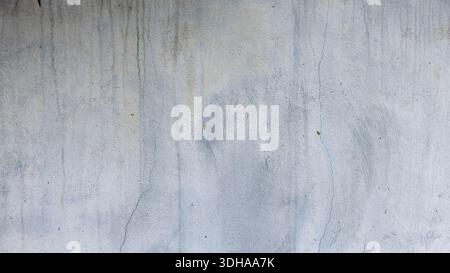 A high-resolution image of a distressed, weathered concrete wall featuring fine cracks, vertical water stains, and a rough, textured surface in shades Stock Photo