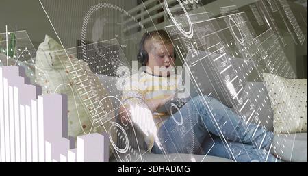 Sitting boy wearing yellow long-sleeve shirt, using tablet at home on sofa with headset, AR overlay Stock Photo