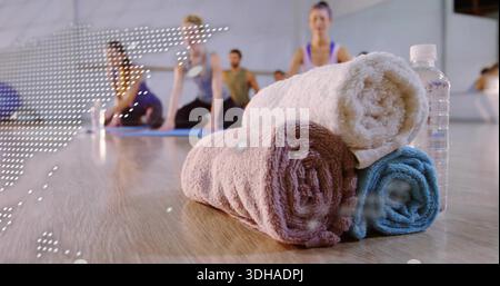 Stacking three rolled towels and water bottle on yoga studio floor, with mats, people in activewear Stock Photo
