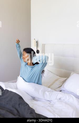 Upholstered tufted headboard is framing white duvet and pillows on bed with bedside lamp Stock Photo