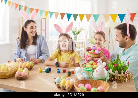 Happy family wearing bunny ears, decorating colorful eggs together at home in bright festive room. Stock Photo