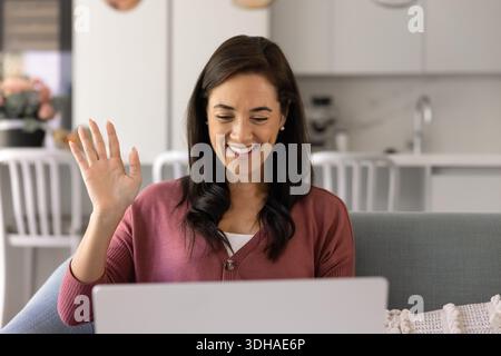 Happy woman sitting on sofa, waving, start video conference Stock Photo